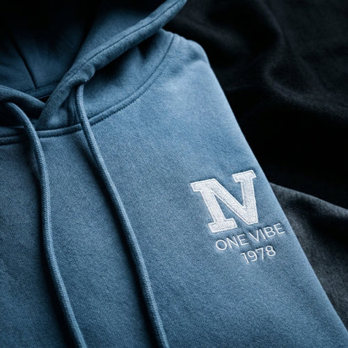 Detail van geborduurd One Vibe 1978 logo wit op babyblauw hoodie.